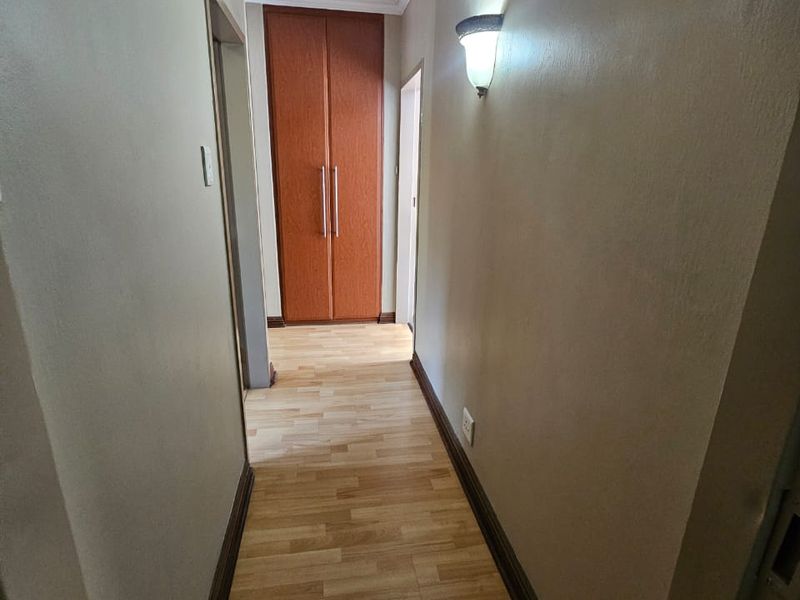 A clean, well-lit hallway featuring laminate flooring, a built-in storage cupboard, and decorative cornice detailing.