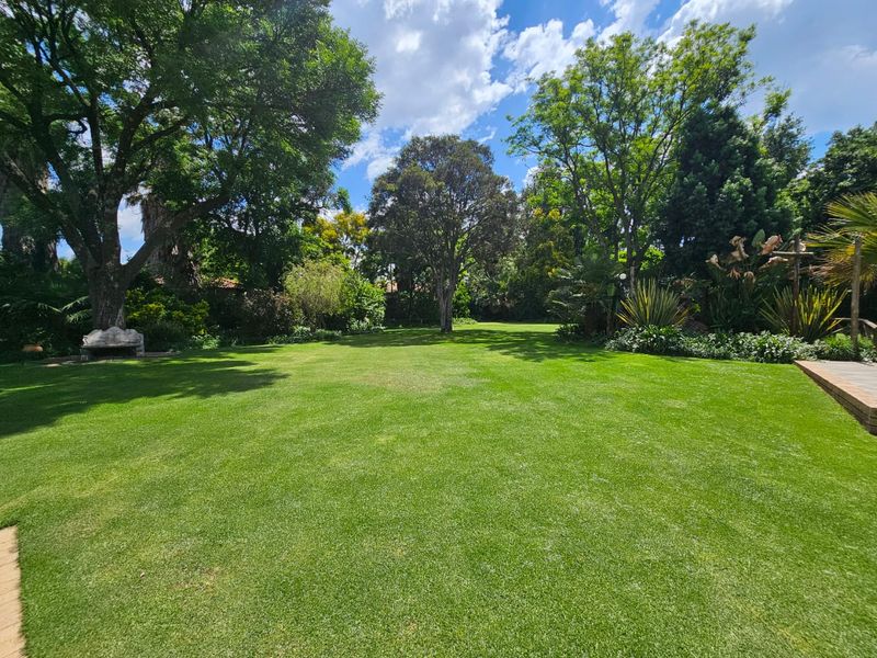 A spacious, well-maintained garden featuring a large, manicured lawn surrounded by mature trees and established landscaping.
