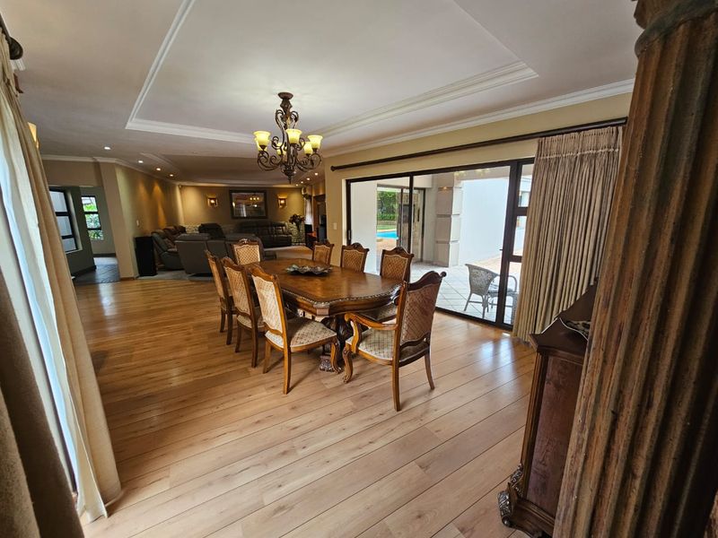 Spacious open-plan dining and living area featuring hardwood flooring, recessed ceiling details, and large sliding glass doors leading to an outdoor patio.