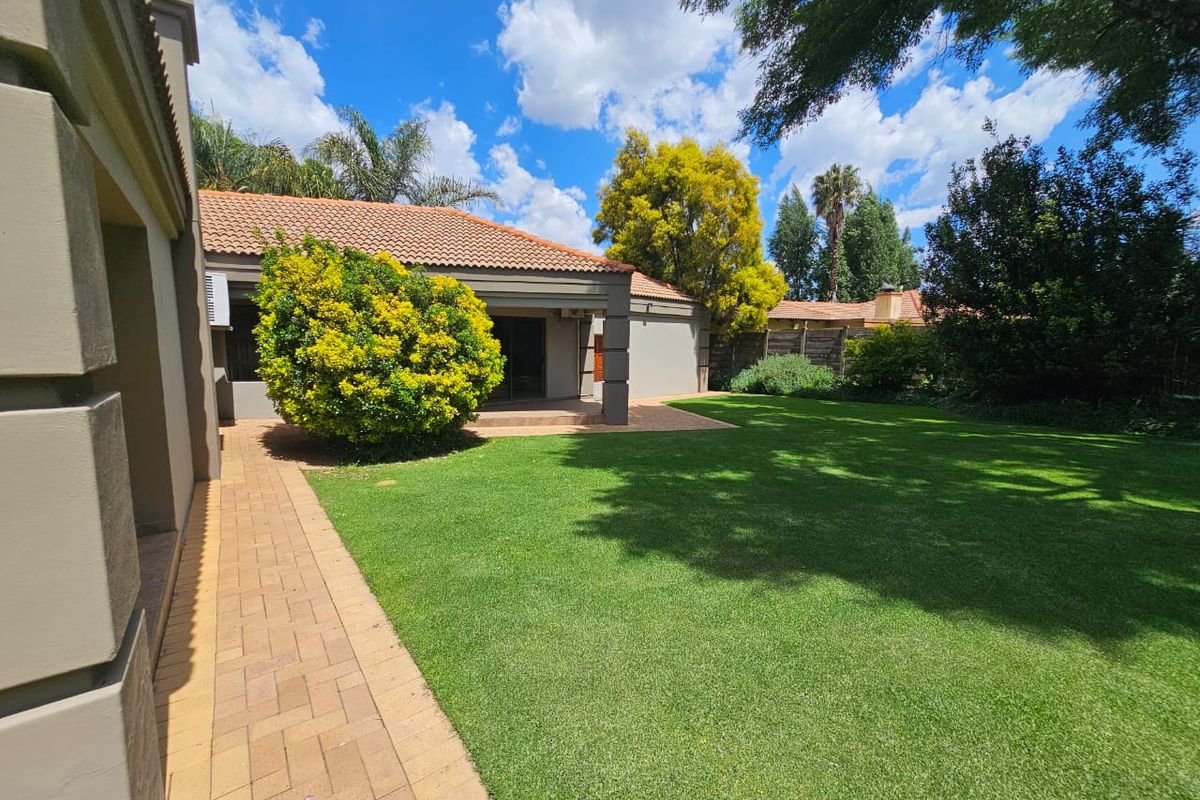 A well-maintained rear garden featuring a lush green lawn, a paved walkway, and a covered patio area attached to the main house structure.