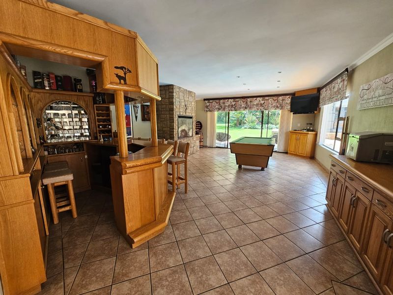 Spacious entertainment room featuring a built-in wooden bar, stone fireplace, and large sliding glass doors opening to the garden.