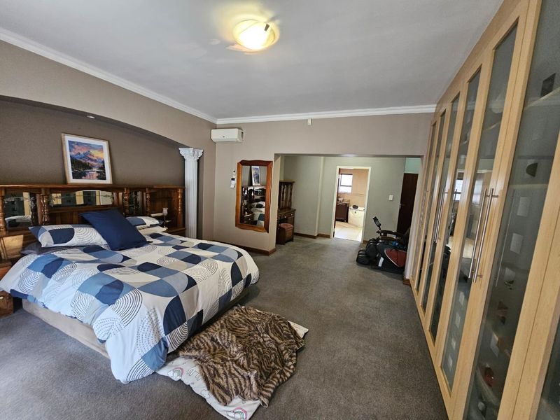 Spacious bedroom featuring extensive built-in cupboards, carpeted flooring, and an integrated air conditioning unit, with an adjoining en-suite bathroom area.