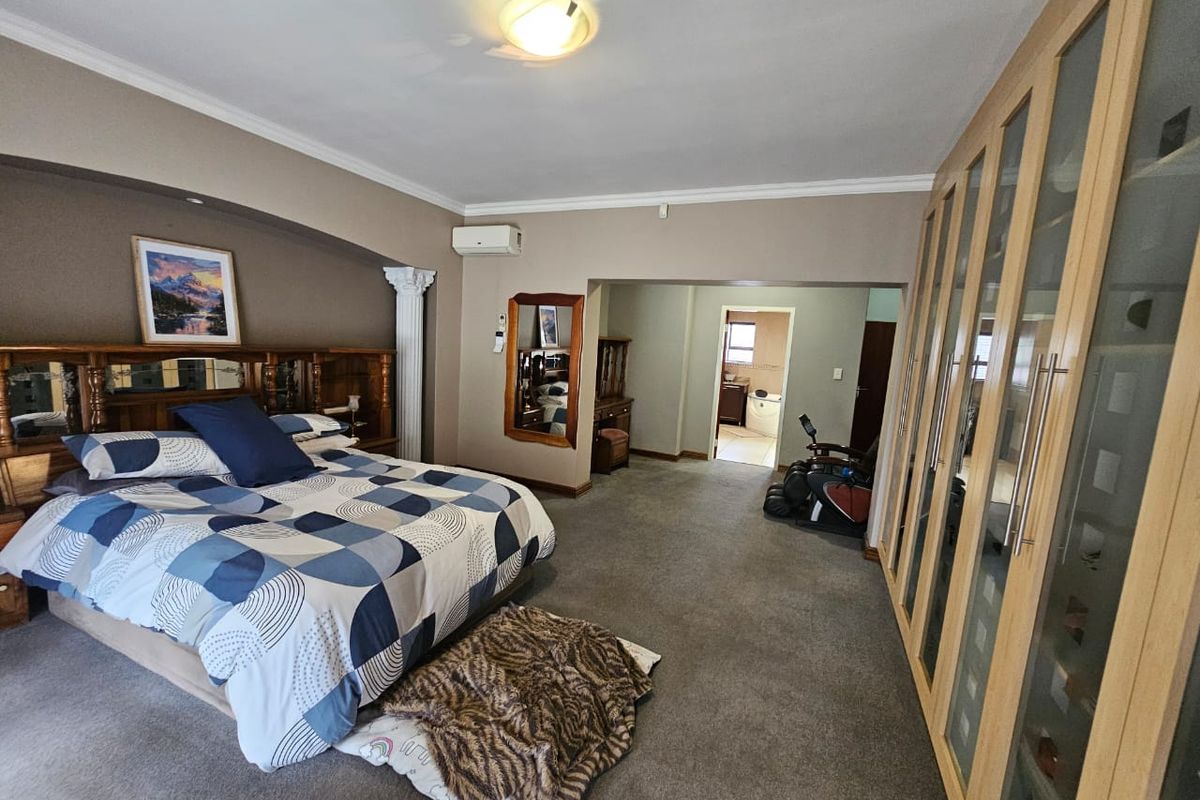 Spacious bedroom featuring extensive built-in cupboards, carpeted flooring, and an integrated air conditioning unit, with an adjoining en-suite bathroom area.