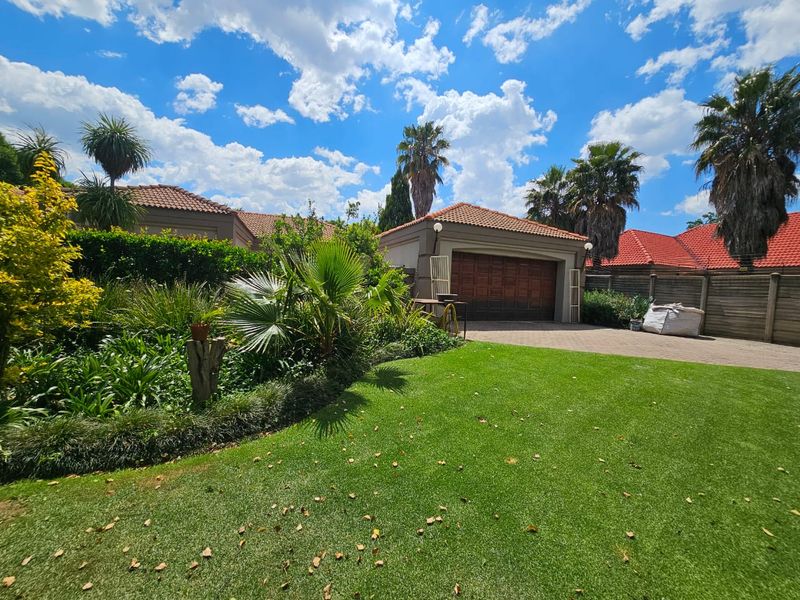 A well-maintained front exterior view featuring a paved driveway, double garage, and a lush, landscaped garden with mature trees.