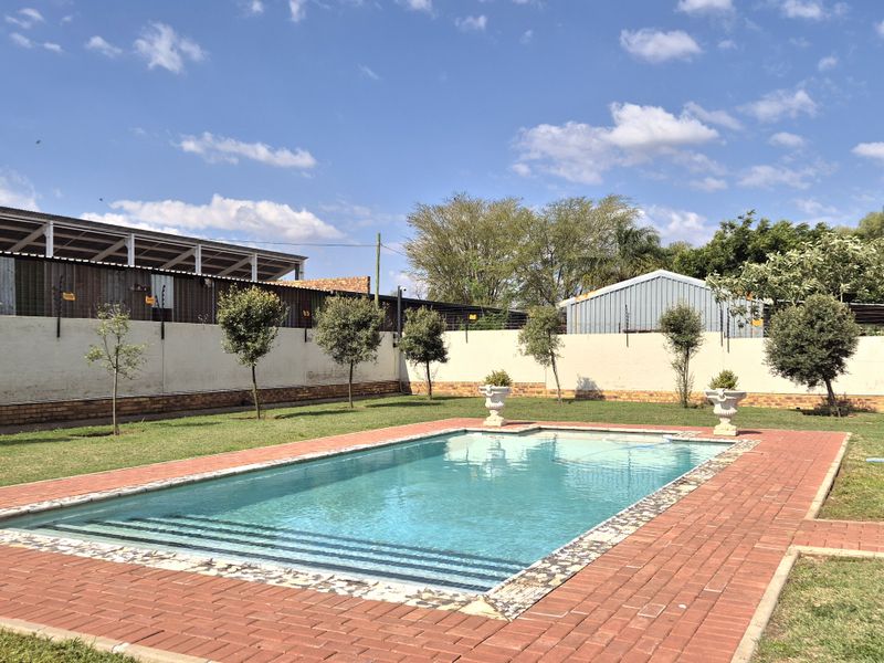 Outdoor pool area featuring a rectangular swimming pool with brick paved surround, enclosed by a perimeter wall with electric fencing.