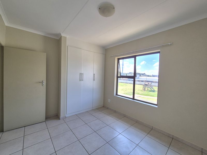 A bright, empty bedroom featuring neutral tiled flooring, built-in cupboards, and a large window providing natural light and exterior views.