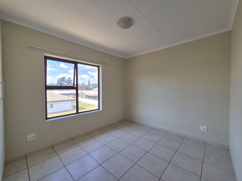 A bright, empty bedroom featuring neutral wall paint, tiled flooring, and an aluminium-framed window providing natural light.