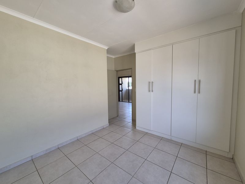 A clean, empty bedroom featuring neutral tiled flooring, built-in white cupboards, and a simple ceiling light fixture.