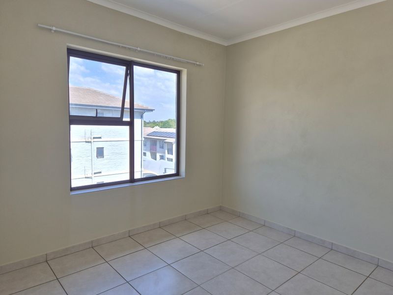 A bright, empty bedroom featuring neutral wall paint, tiled flooring, and a large aluminium-framed window with a curtain rod.