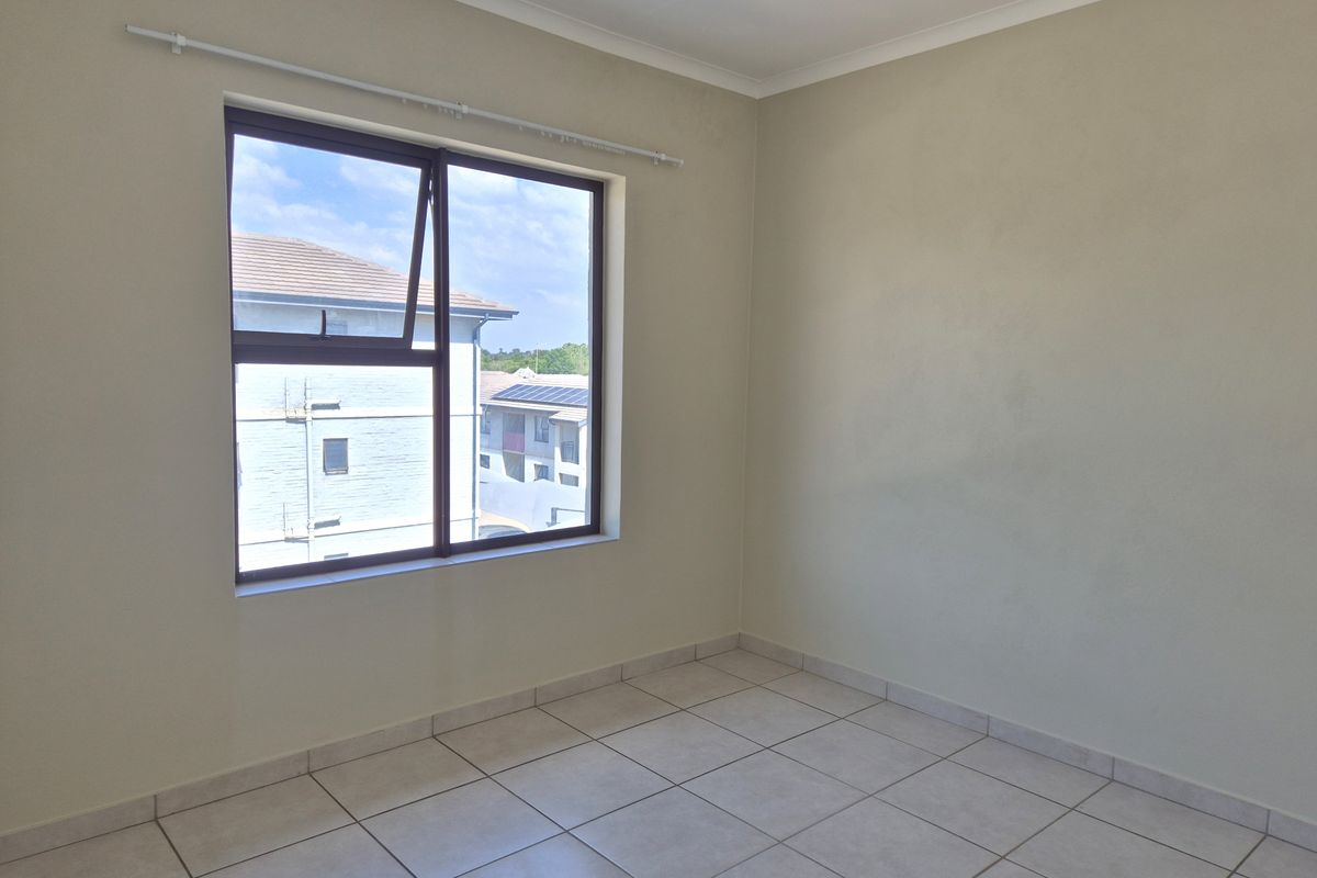A bright, empty bedroom featuring neutral wall paint, tiled flooring, and a large aluminium-framed window with a curtain rod.