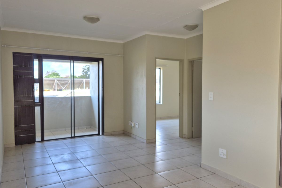 An empty, open-plan living area featuring neutral tiled flooring, a sliding glass door leading to a balcony, and access to adjacent rooms.
