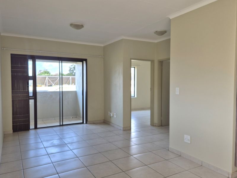 An empty, open-plan living area featuring neutral tiled flooring, a sliding glass door leading to a balcony, and access to adjacent rooms.