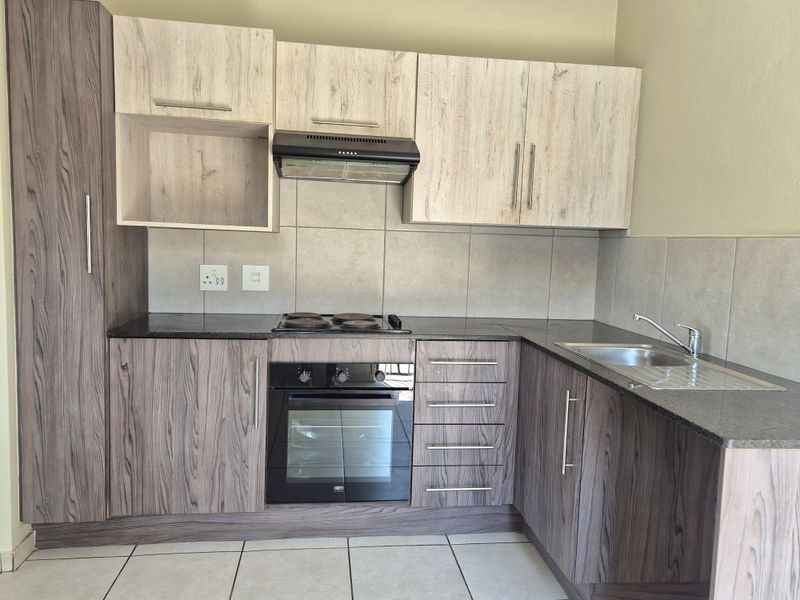 Modern kitchen featuring wood-grain cabinetry, dark laminate countertops, built-in oven, electric hob, extractor fan, and a stainless steel sink with tiled backsplash.