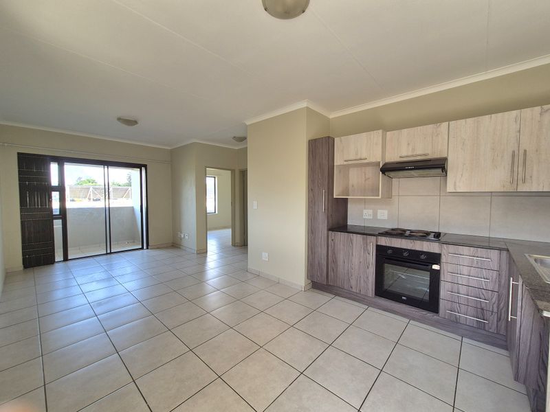 Open-plan living area featuring a modern kitchen with built-in appliances, tiled flooring, and access to a private balcony through sliding glass doors.