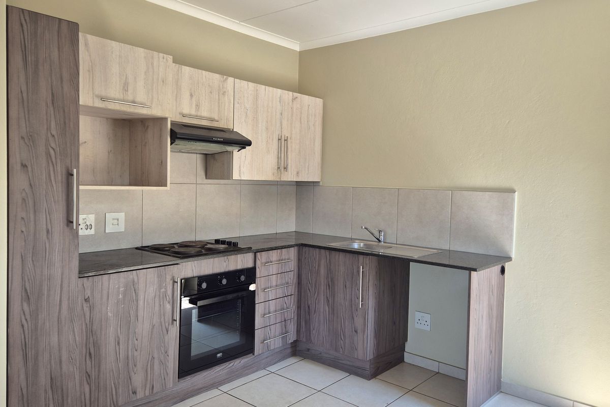 A clean and modern kitchen featuring wood-grain cabinetry, dark laminate countertops, a built-in oven, electric hob, and tiled flooring.