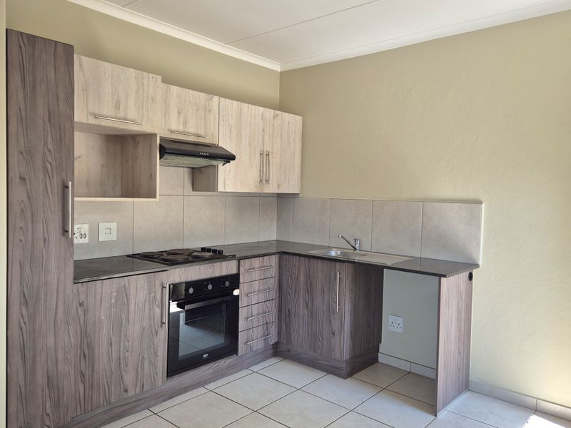 A clean and modern kitchen featuring wood-grain cabinetry, dark laminate countertops, a built-in oven, electric hob, and tiled flooring.