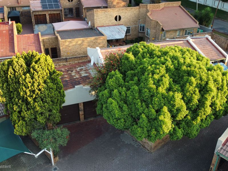 Aerial view of a residential property featuring brick-paved driveway, multiple garage units, and mature trees within a suburban estate setting.