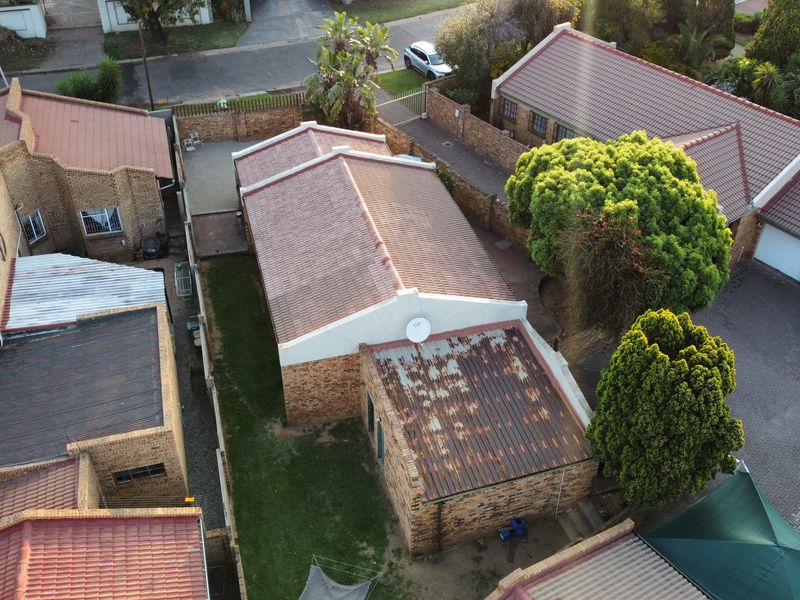 Aerial view of a residential property showing multiple brick structures, tiled roofing, and a small garden area with visible roof maintenance required.