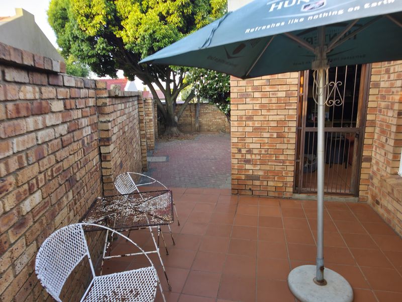 A paved outdoor patio area featuring brick boundary walls, tiled flooring, and direct access to the home through a security gate.