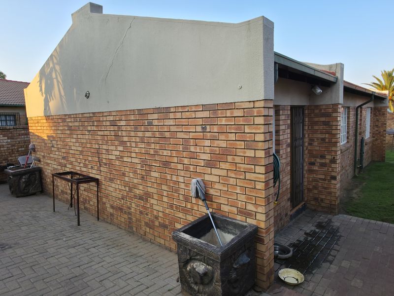 A rear exterior view of the property featuring a face brick facade, paved courtyard area, and a small lawn.