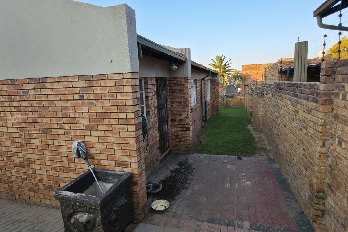 A side view of the property featuring face brick walls, a paved walkway, and a small lawn area enclosed by brick boundary walls.