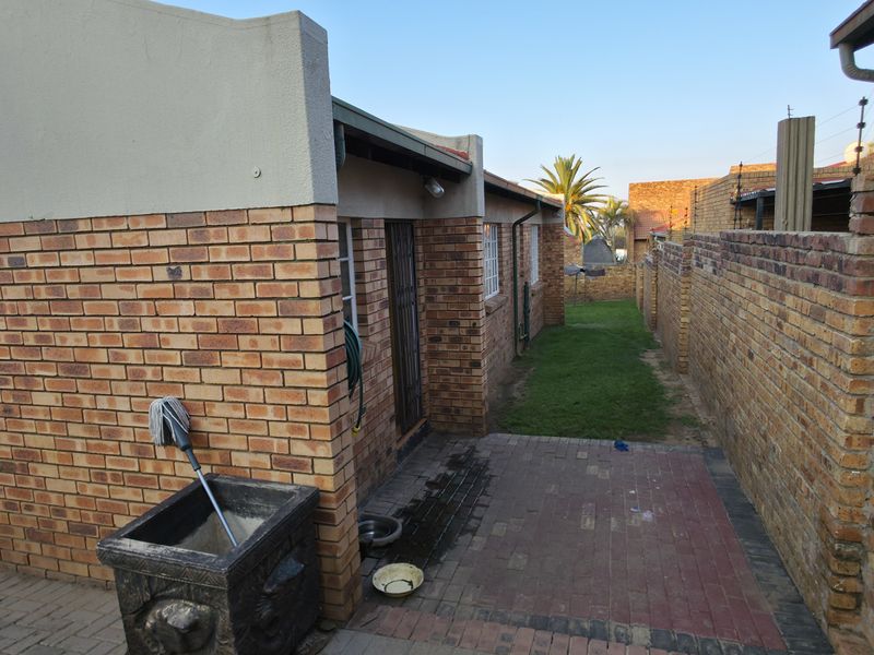 A side view of the property featuring face brick walls, a paved walkway, and a small lawn area enclosed by brick boundary walls.