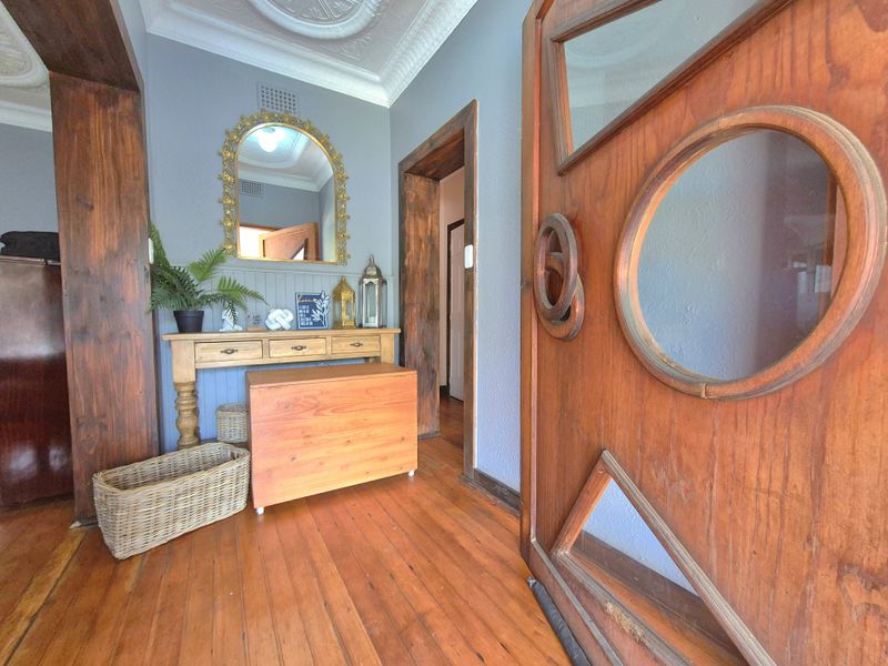 Welcoming entrance hall featuring original timber flooring, ornate ceiling detailing, and a distinctive timber front door with unique glass panel inserts.