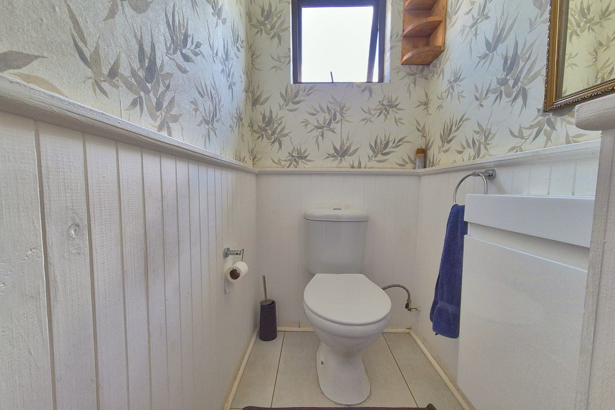 A compact bathroom featuring wainscoting, patterned wallpaper, a white toilet, and a vanity unit with tiled flooring.