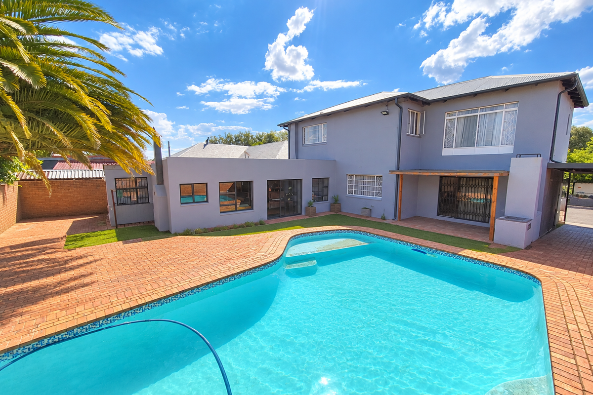 Rear exterior view featuring a swimming pool, brick paved patio area, and a built-in braai under a timber pergola.