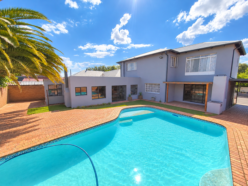 Rear exterior view featuring a swimming pool, brick paved patio area, and a built-in braai under a timber pergola.