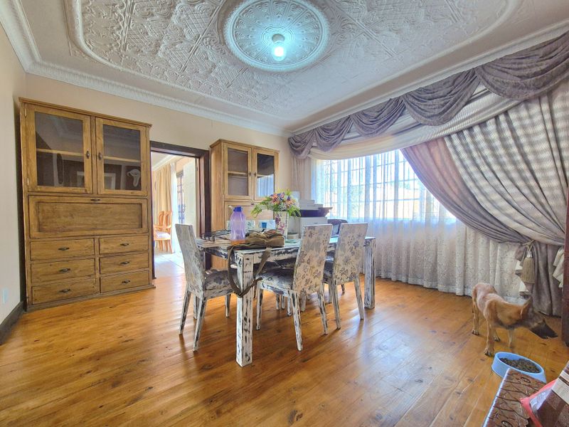 A dining room featuring original hardwood flooring, an ornate plaster ceiling rose, and a large bay window with natural light.