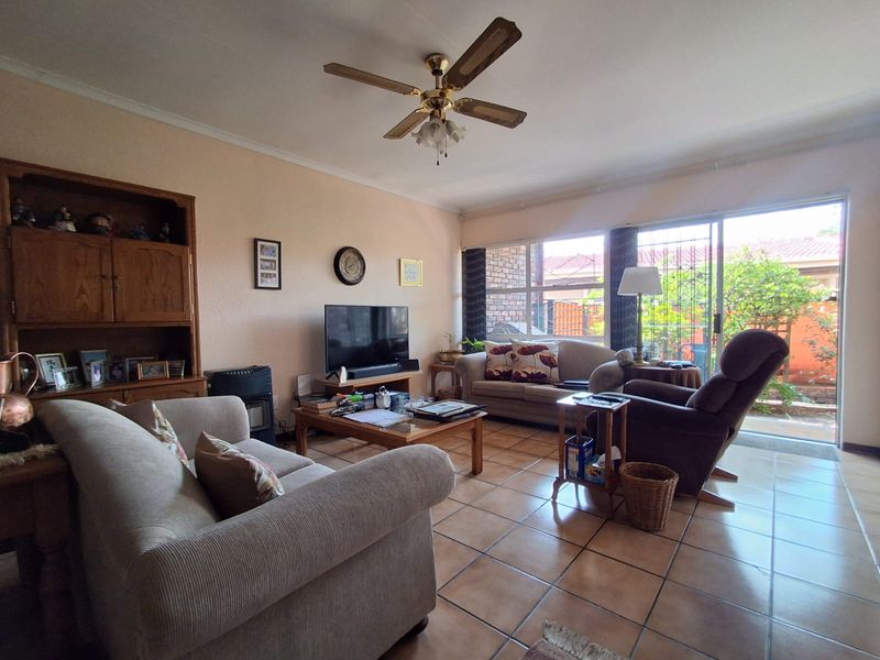 A comfortable living room featuring tiled flooring, a ceiling fan, and large sliding glass doors that provide access to the outdoor area.