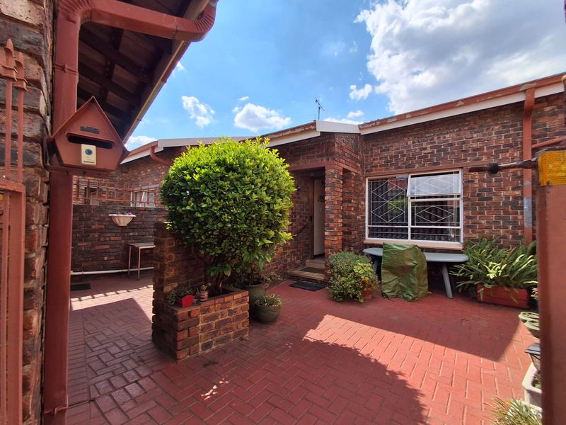 Front entrance area of a townhouse featuring face brick construction, paved courtyard, and secure window bars.