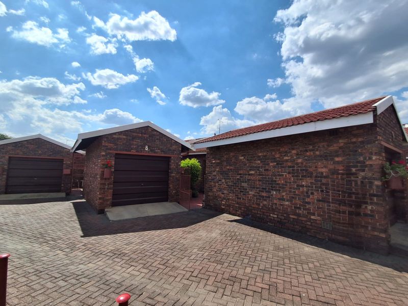 Exterior view of a townhouse complex featuring face brick construction, tiled roofing, and a paved driveway with individual garage access.