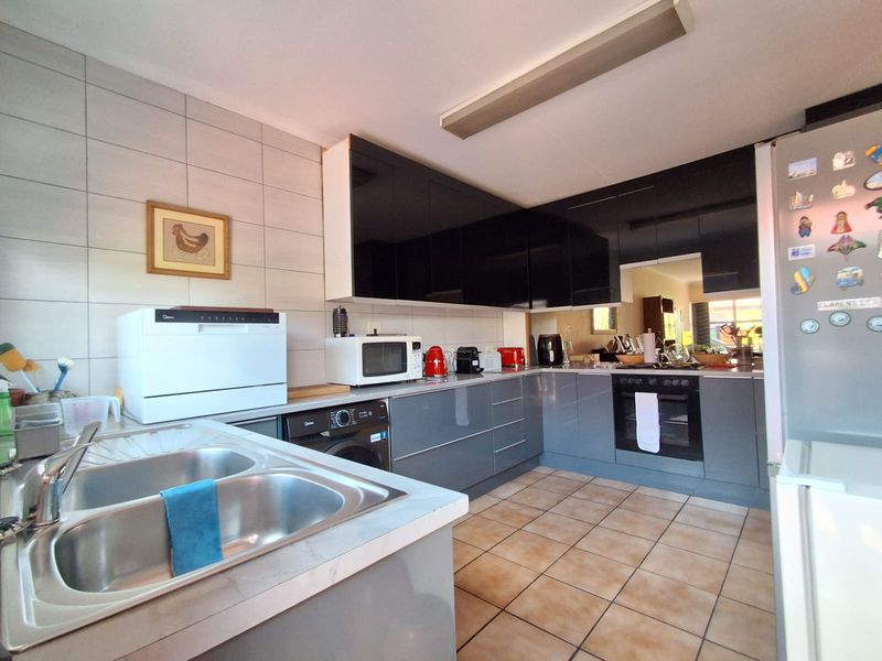 Modern kitchen featuring glossy grey and black cabinetry, tiled backsplash, built-in oven, and a double bowl stainless steel sink.