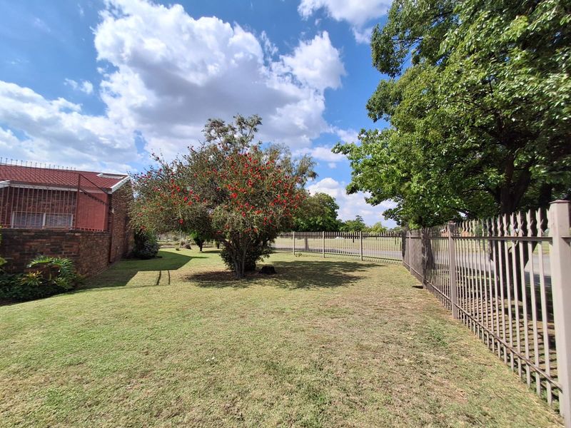 A well-maintained garden area featuring a manicured lawn, mature trees, and secure metal perimeter fencing with a brick boundary wall.