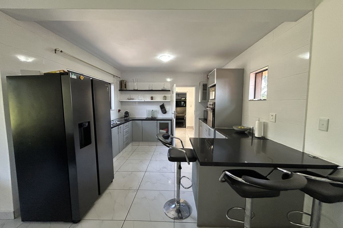 A modern kitchen featuring sleek grey cabinetry, dark stone countertops, built-in appliances, and polished white tiled flooring with a breakfast bar area.