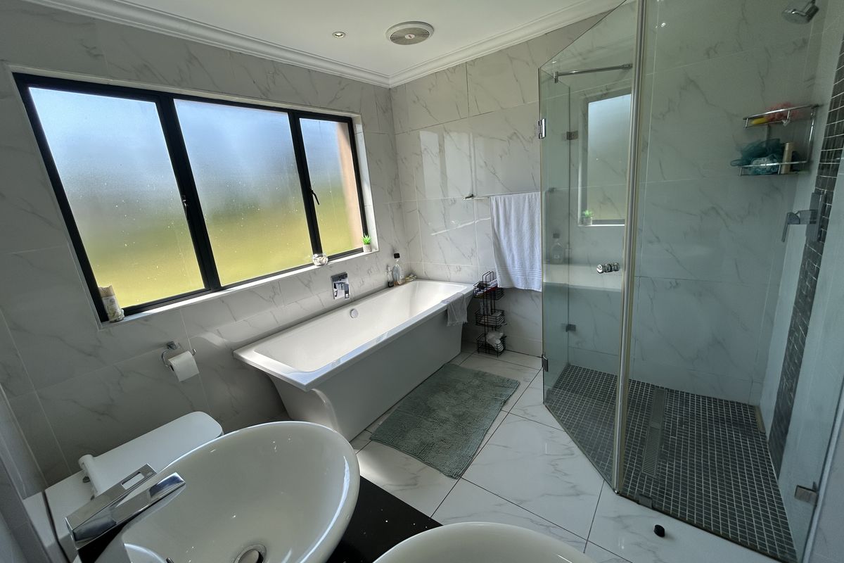 Modern bathroom featuring a double vanity, a sleek freestanding bathtub, and a spacious glass-enclosed shower with contemporary marble-look tiling.