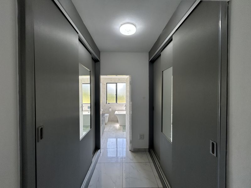 A clean, modern hallway featuring built-in sliding door cupboards with mirrored panels and polished tiled flooring, leading directly into an adjacent bathroom.