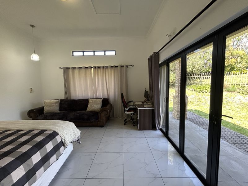 Spacious bedroom featuring large format marble-look floor tiles and expansive black aluminium sliding stacker doors providing direct access to the outdoor patio and garden.