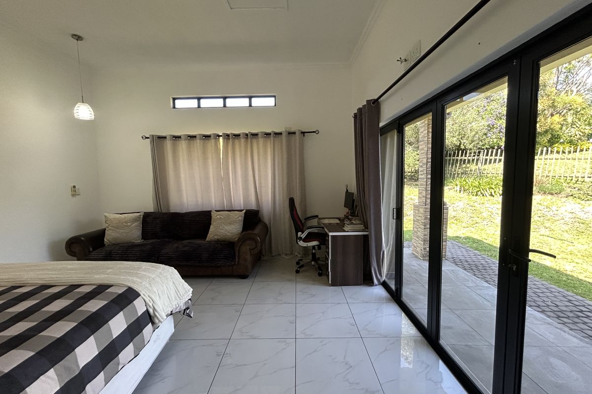 Spacious bedroom featuring large format marble-look floor tiles and expansive black aluminium sliding stacker doors providing direct access to the outdoor patio and garden.