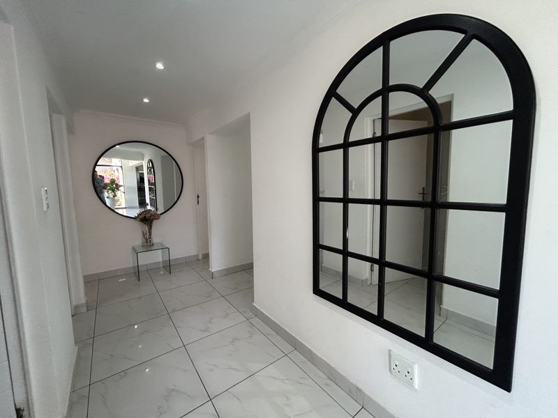 A bright and clean hallway featuring modern white porcelain floor tiles and recessed downlighting, providing a neutral and well-maintained transition space.