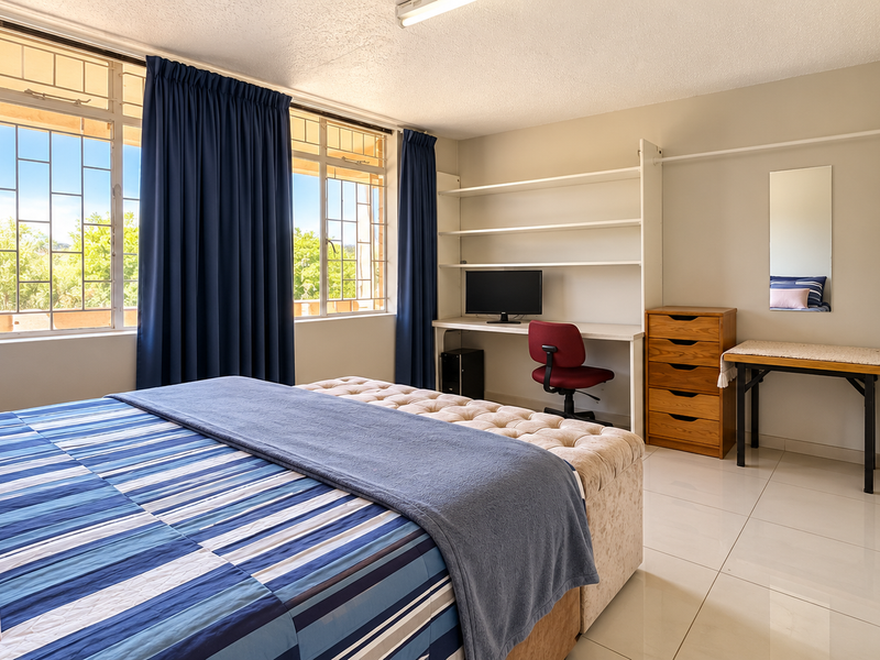 Spacious bedroom featuring tiled flooring, built-in desk with shelving, and a large built-in wardrobe, offering ample storage and natural light.