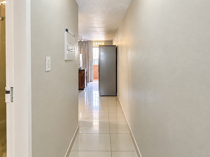 A bright hallway with polished tile flooring, leading towards an open living area, with a glimpse of an adjacent bathroom featuring a vanity and shower.