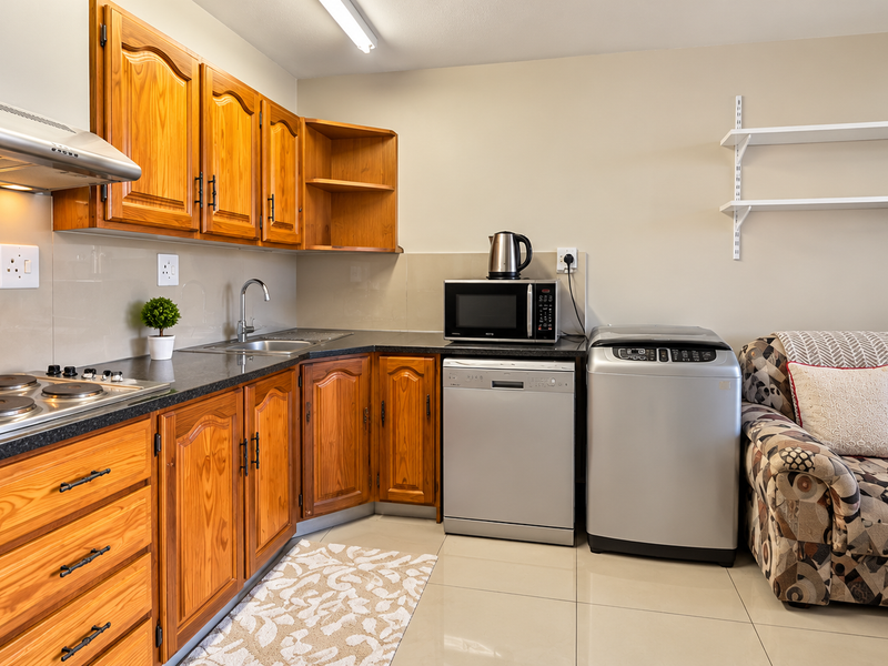 Open-plan kitchen area featuring wooden cabinetry, integrated hob, extractor fan, and tiled flooring, seamlessly flowing into the adjacent living space.