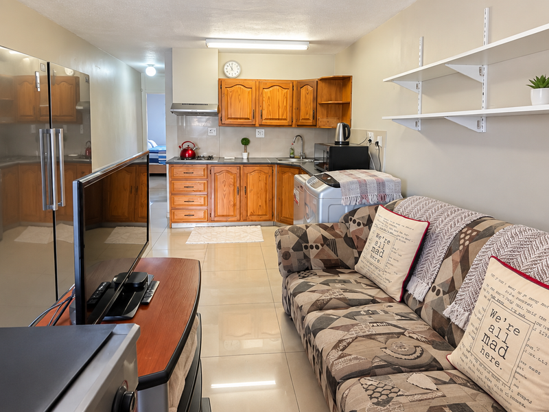 Open-plan living area featuring a compact kitchen with wooden cabinetry, tiled flooring, and wall-mounted shelving, creating a functional and integrated living space.