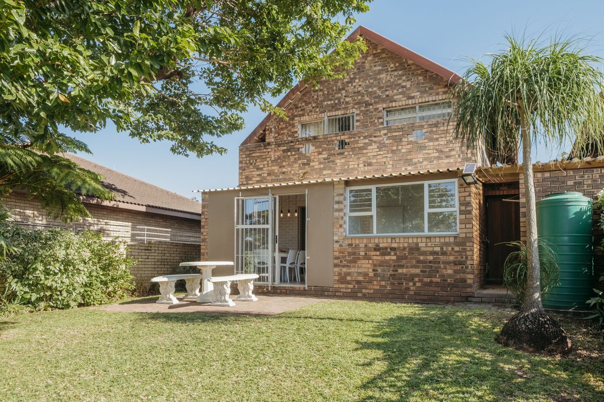 Rear view of a double-storey face brick townhouse featuring a private garden, paved patio area, and a water storage tank.