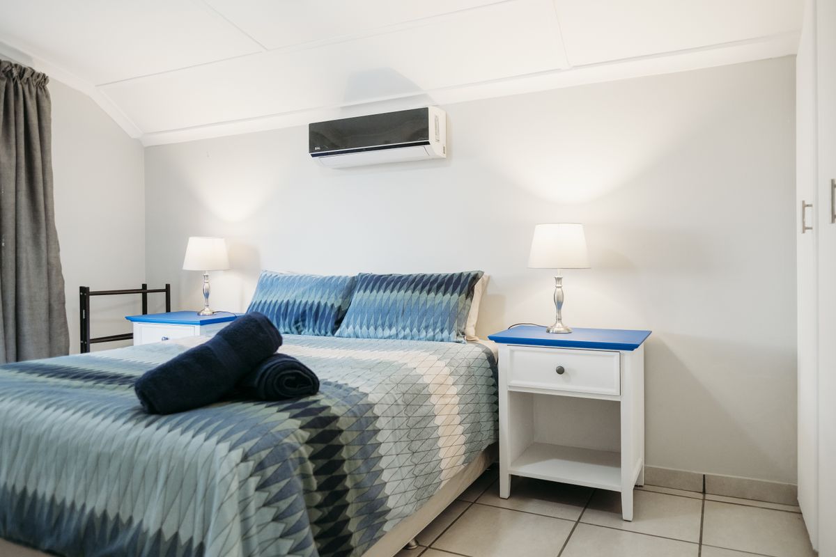 A well-maintained bedroom featuring tiled flooring, a wall-mounted air conditioning unit, and built-in storage.