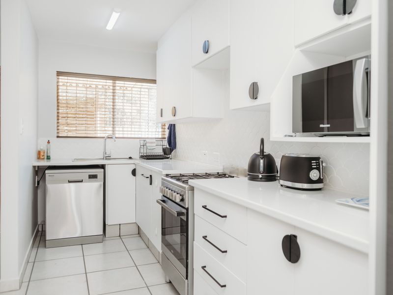 A clean, modern kitchen featuring white cabinetry, a gas stove, built-in microwave, and tiled finishes, offering a bright and functional workspace.