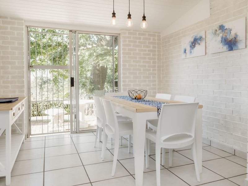Bright dining area featuring white painted exposed brick walls, tiled flooring, and a sliding glass door providing access to the outdoor space.